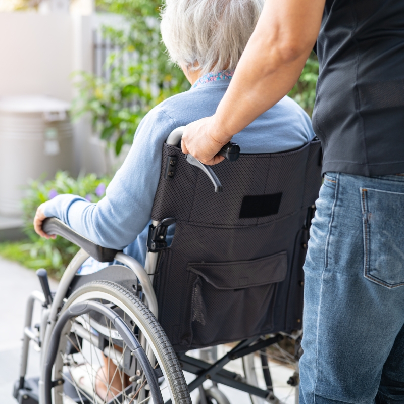 Carer assisting elderly woman in wheelchair outdoors – NDIS Short-Term Respite Sydney support in action.